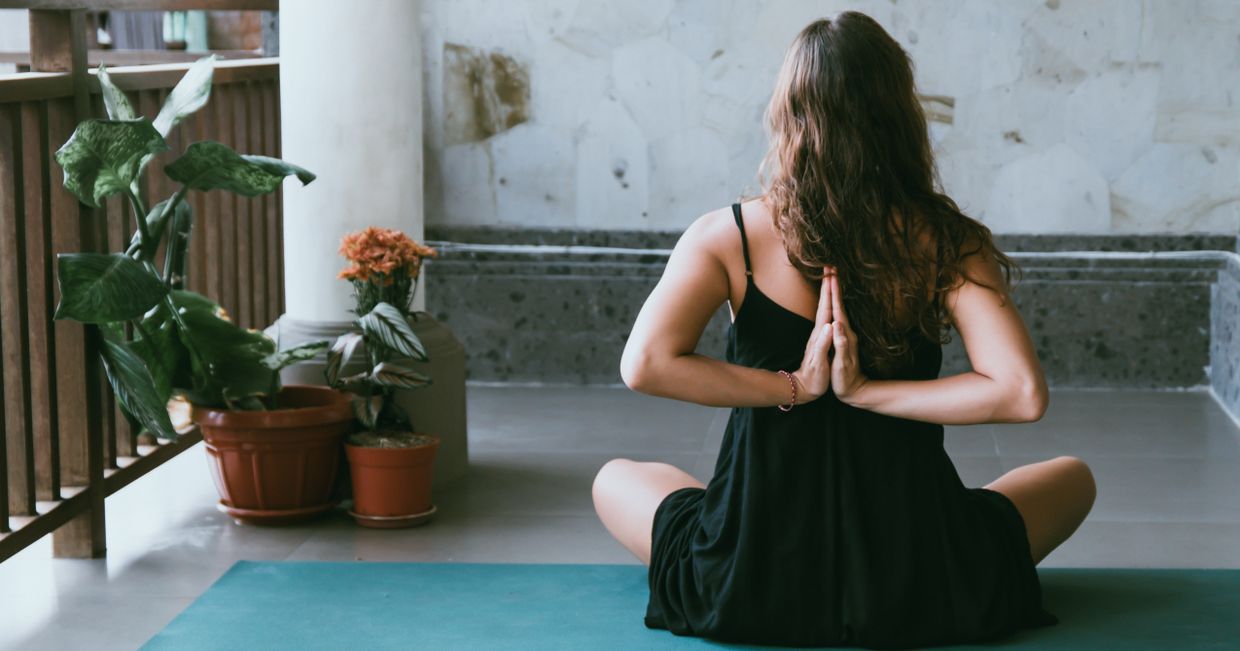 Dziewczyna siedząca na macie na balkonie, ćwicząca jogę (fot. Avrielle Suleiman / unsplash.com)