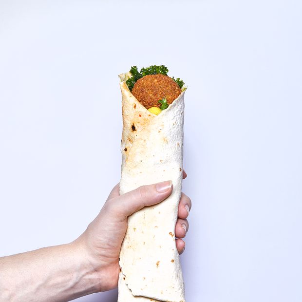 Falafel w picie, z jarmużem i piklami, zawinięty w placek pita – trzymany w dłoni (fot. Maciej Niemojewski)