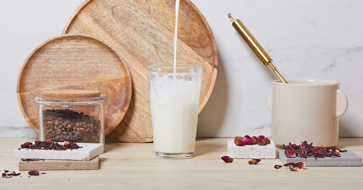 Przygotowywanie kawy, mleko nalewane do wysokiej szklanki, ziarenka kawy i płatki kwiatów (fot. Maciek Niemojewski)