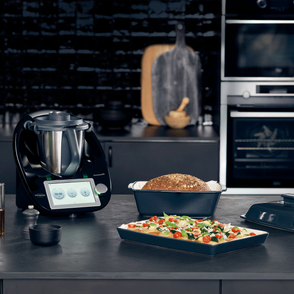 Potrawy i sprzęt kulinarny na kuchennym blacie, czarny model sprzętu agd