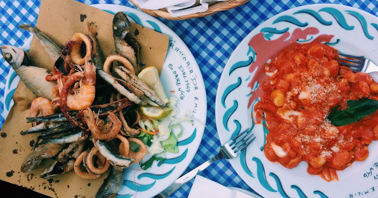 Talerz z owocami morza i talerz z gnocchi, oba ułożone na obrusie w biało- niebieską kratę