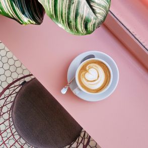Filiżanka kawy na różowym blacie, liść rośliny (fot. Natanja Grun / unsplash.com)