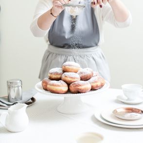 Osoba posypuje pączki cukrem pudrem