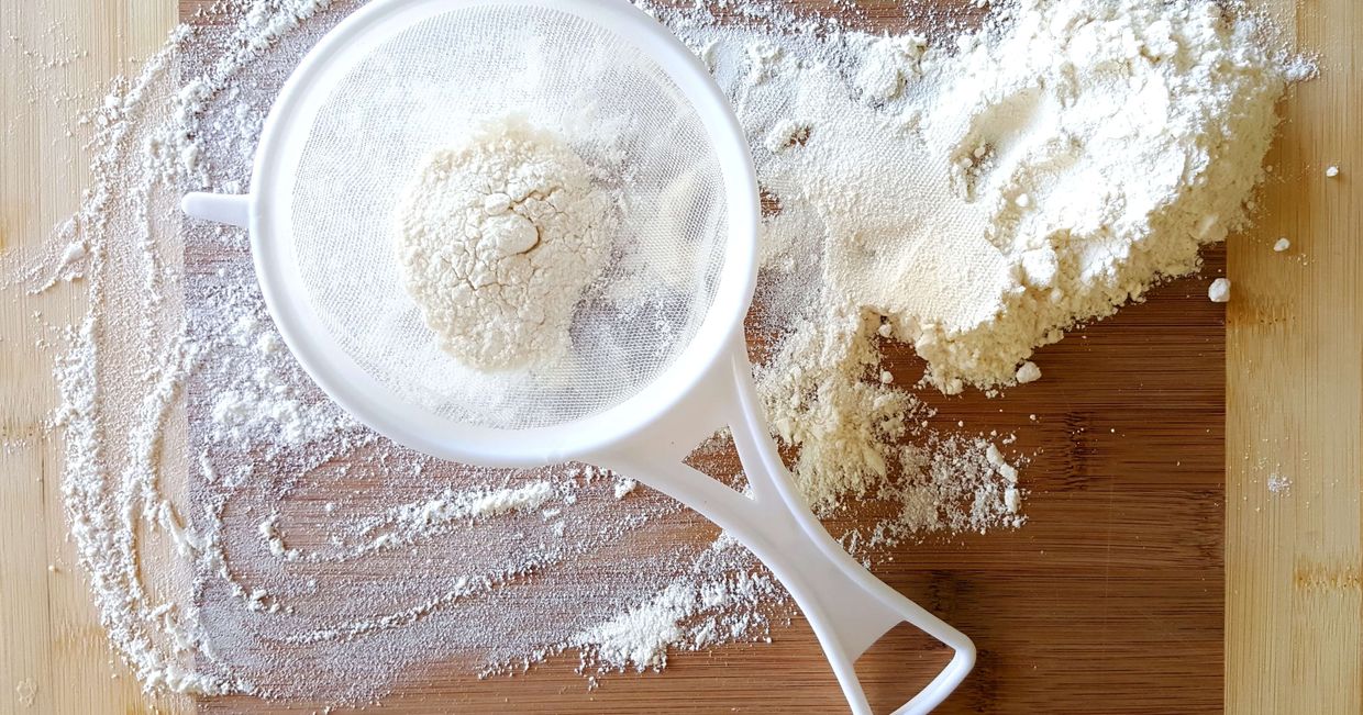 Rozsypana mąka z sitkiem na drewnianym blacie (fot. Vlad Kutepov)